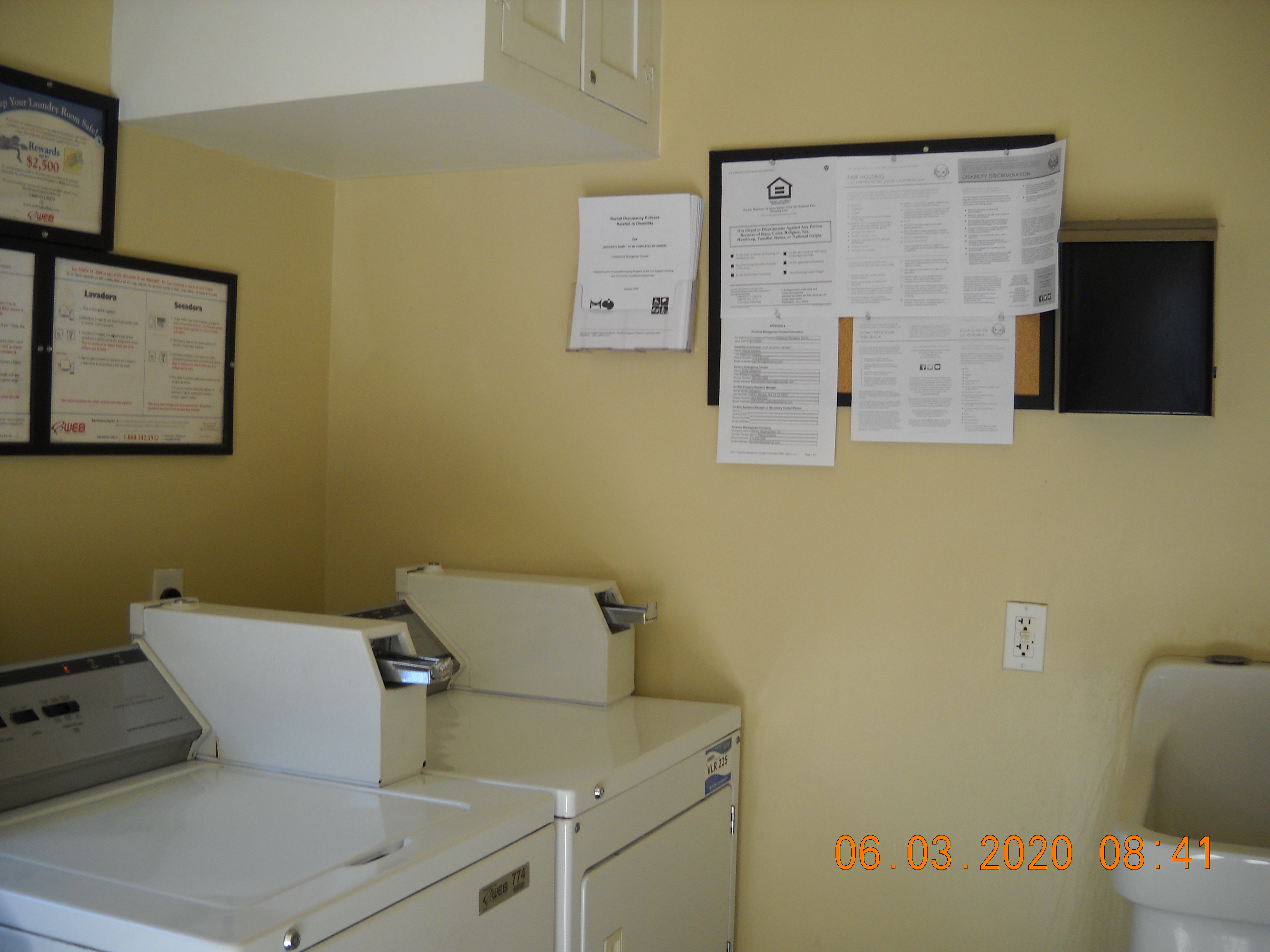Laundry room with two machines and a sink visible.There are multiple signs posted on the wall and a small cabinet that sits overhead.