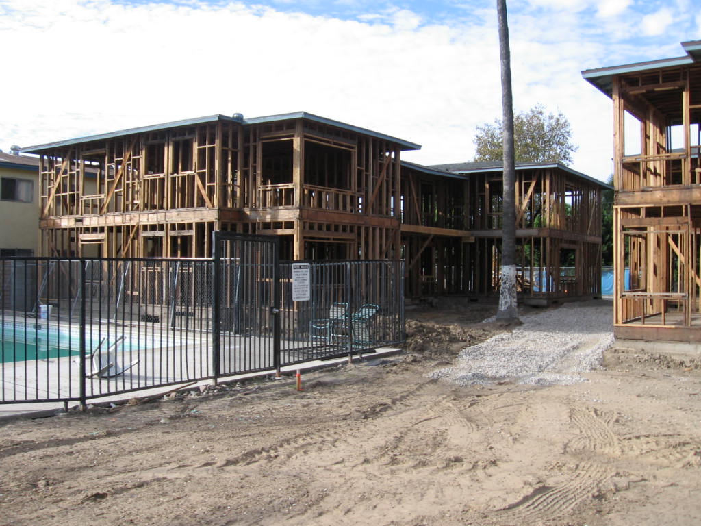 View of building in development. Exposed wood framing. Dirt and gravel paving around builing. Gated pool