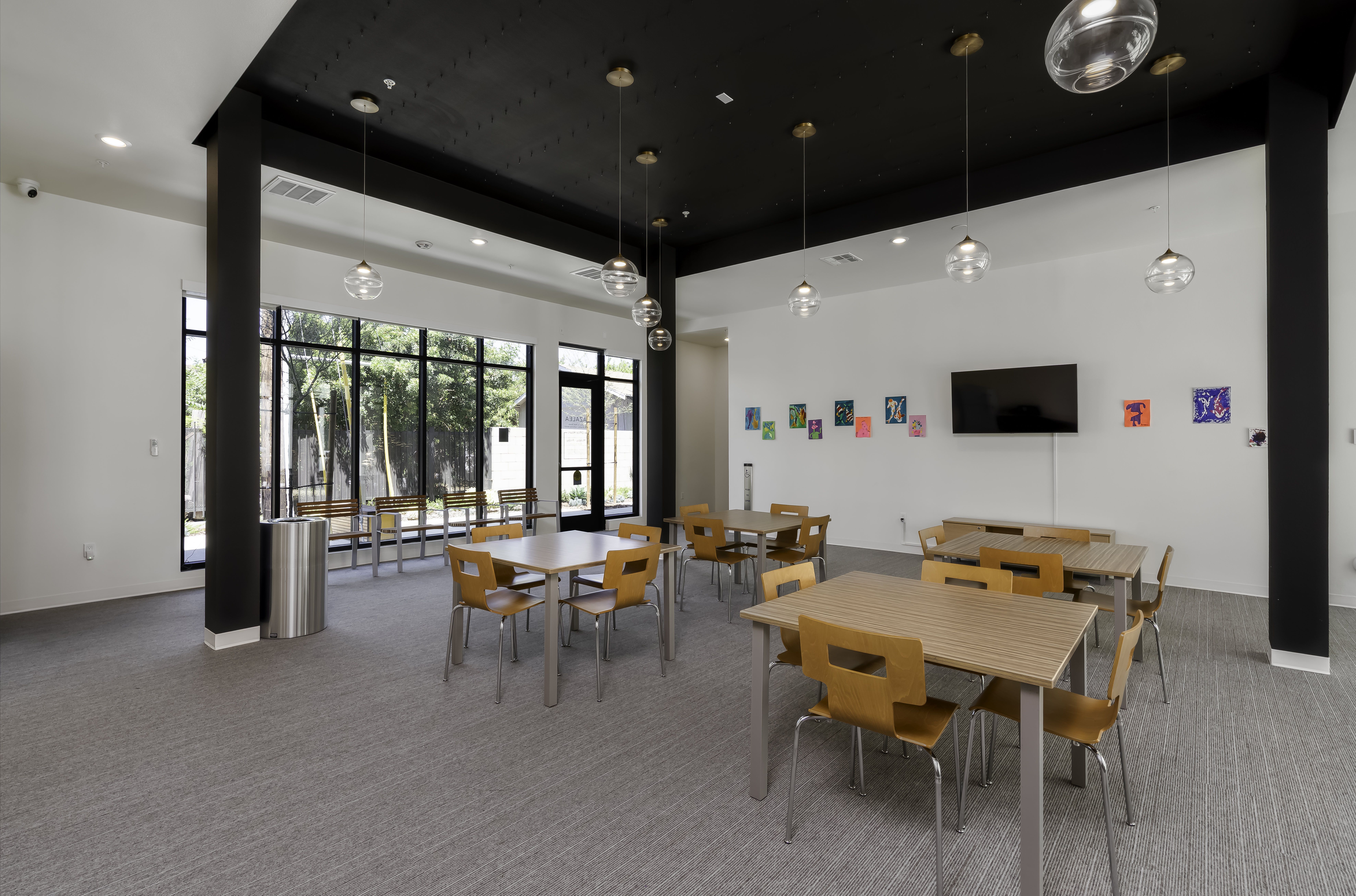 Community Room. Full view of seating area with TV mounted on the wall. The glass wall and door to the left of photo with bench seating up against the glass.