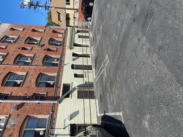 Different view of an outdoor parking lot a old fashioned four story brick building. Ground floor is painted white, and above floors are red. Side of the parking has a railing separating the parking and the building.