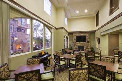 Interior image of Andalucia Senior Apartments common area with many tables with 4 chairs each and fire place