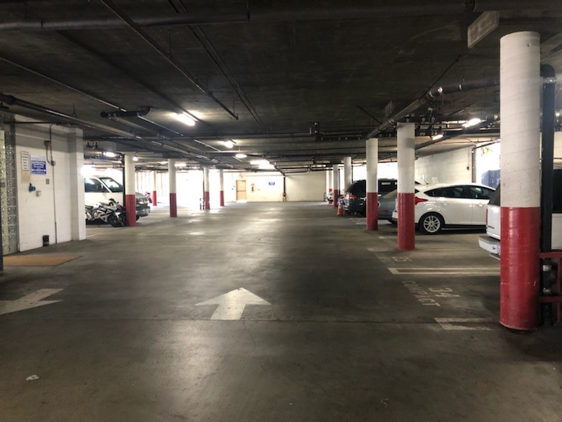 Covered parking garage with multiple space. There are pilars separating spaces which are marked by numbers. In the distance there's a yellow door with a push bar.