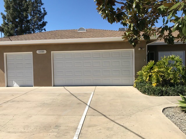Driveway view of a white single car garage door to the left of a white two-car garage door with landscaping to the right.