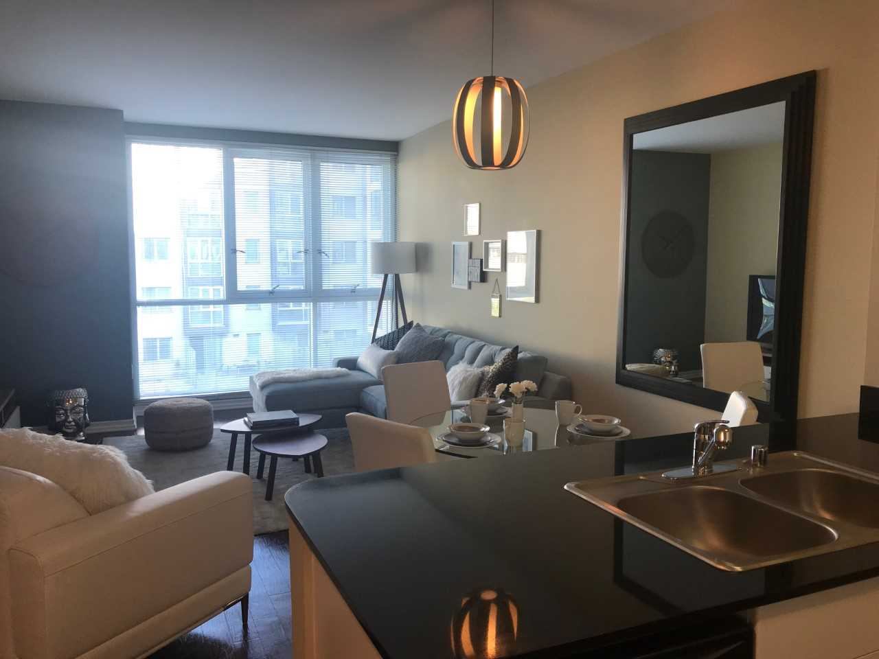 Inside view of a unit's living room. There are couches, coffee table, dining set, and large windows that open multiple ways. Room is adjacent to the kitchen counter with a sink and dishwasher.