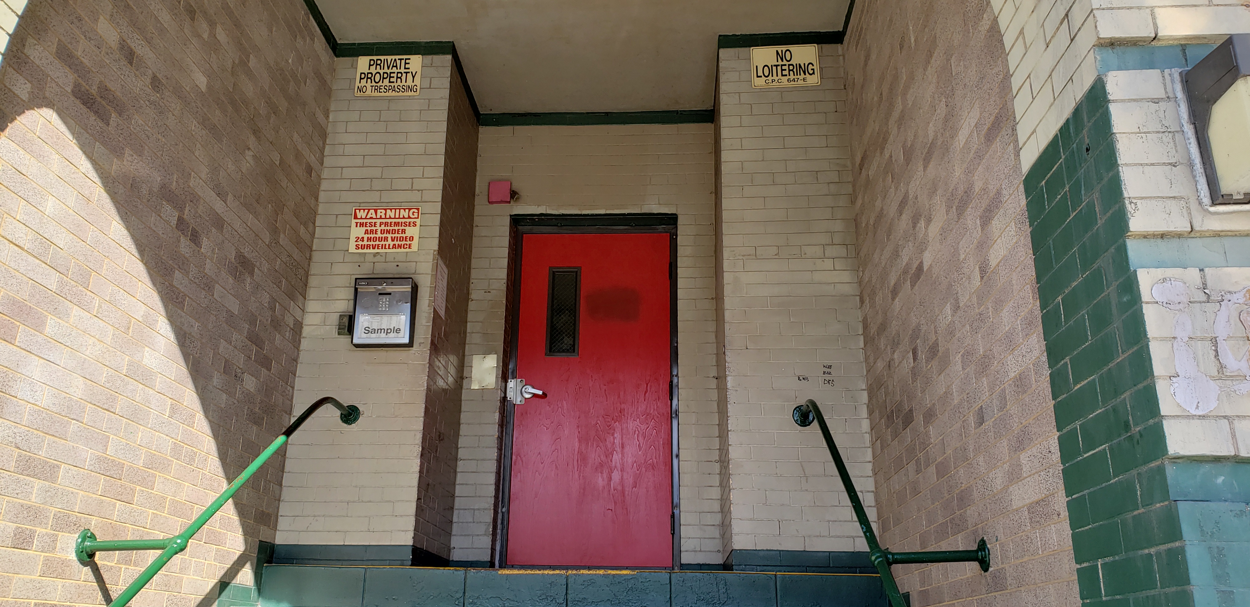 A close up view of the red entrance door to Reno Apartments with brown/stone colored stairs leading up to it.