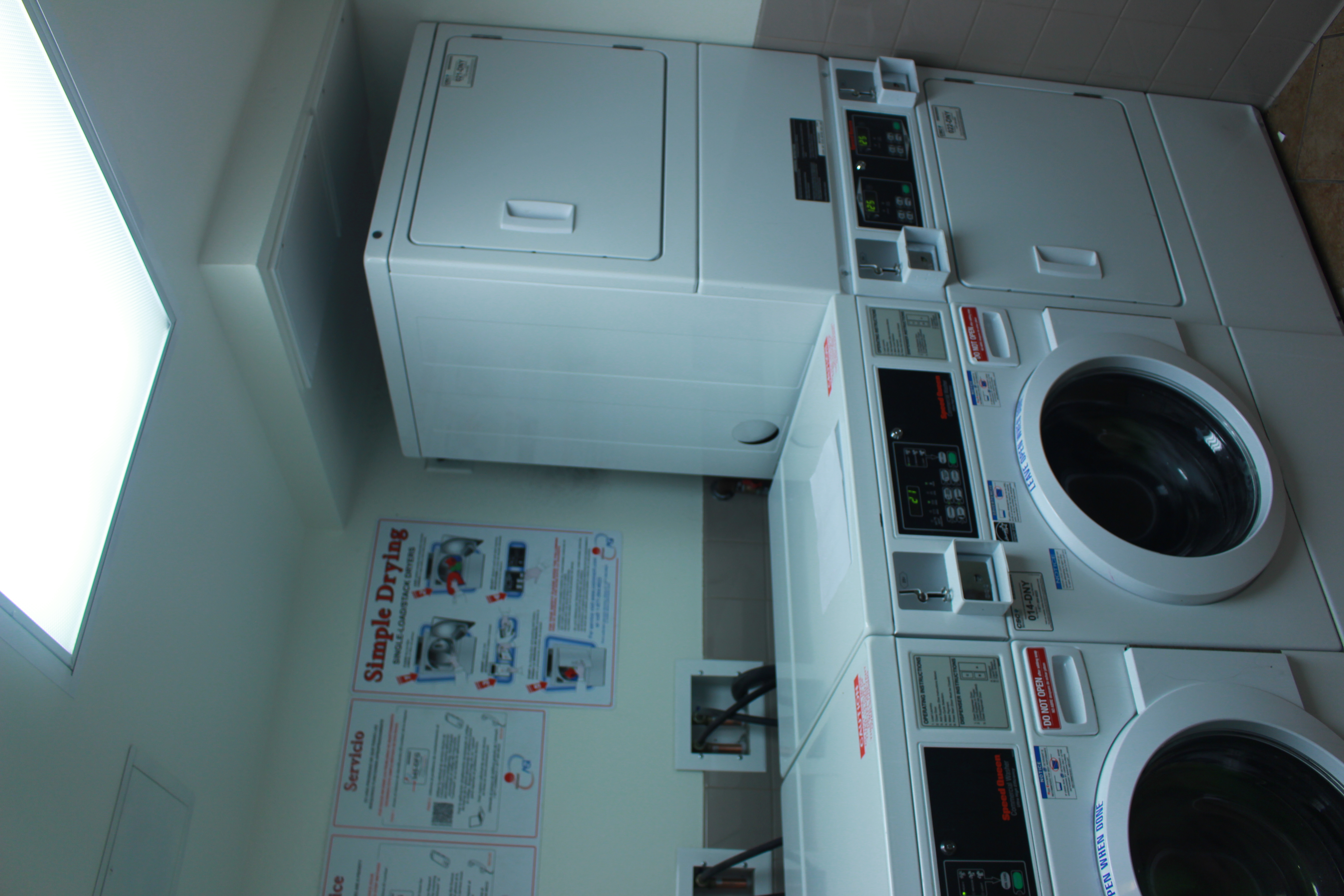 Two white washers and two white dryers, service and instructions signs on the wall.
