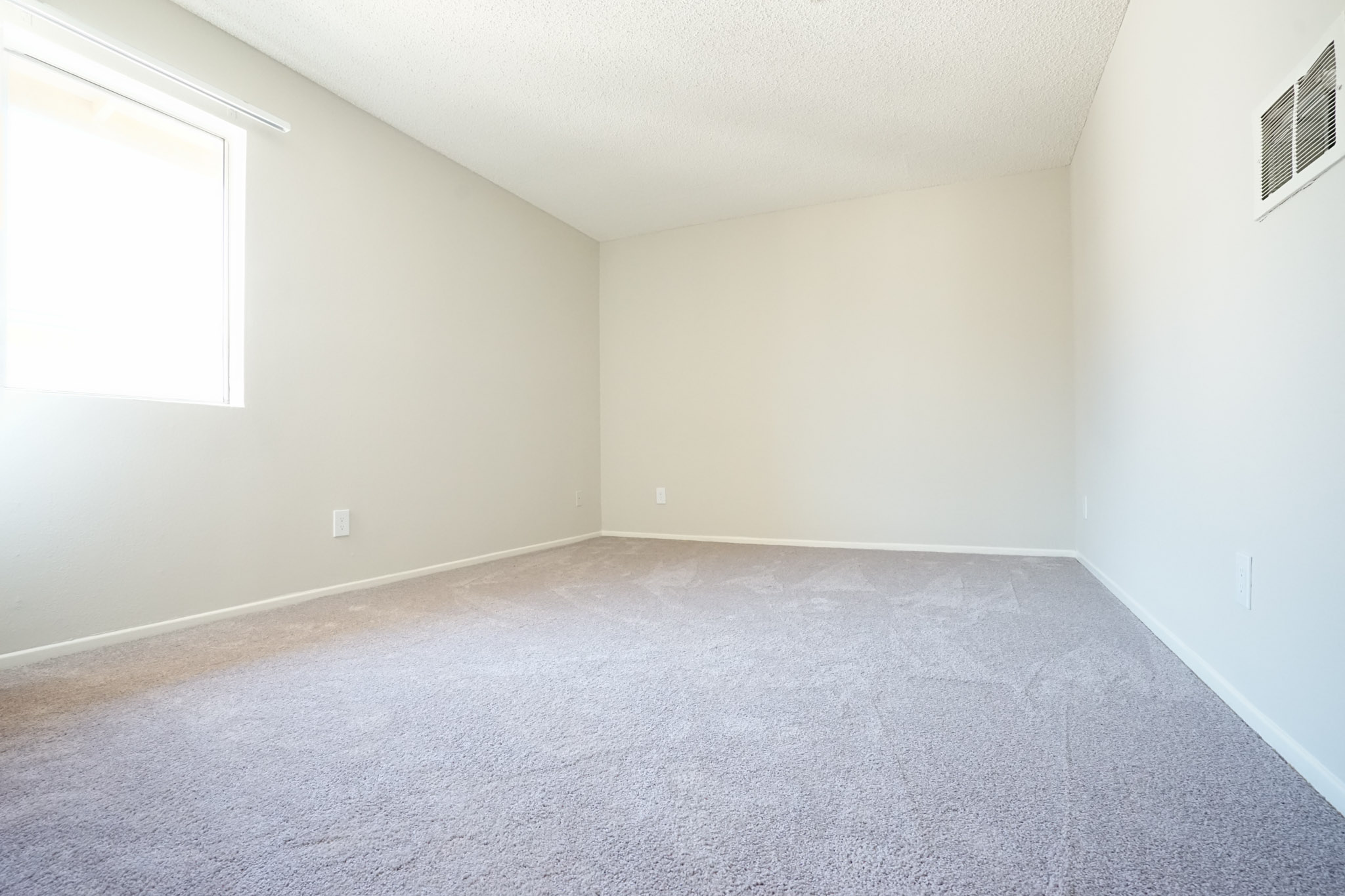 View of a bedroom with carpeted floor and a window with blinds.