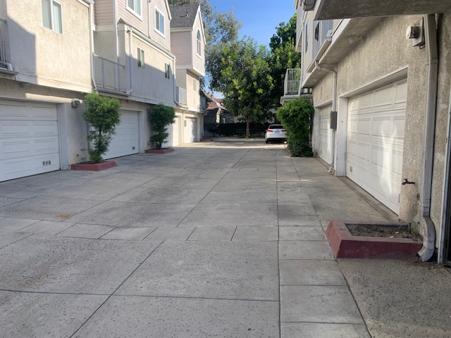 Picture of the back of both buildings with a wide concrete driveway in the middle. Showing the attached garage of each unit facing the driveway.
