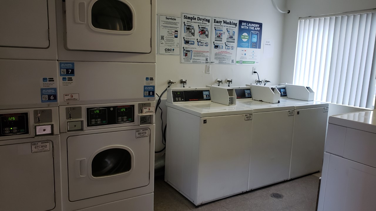 Laundry with multiple machines. There are instruction sigs on the wall. There is a window with blinds.