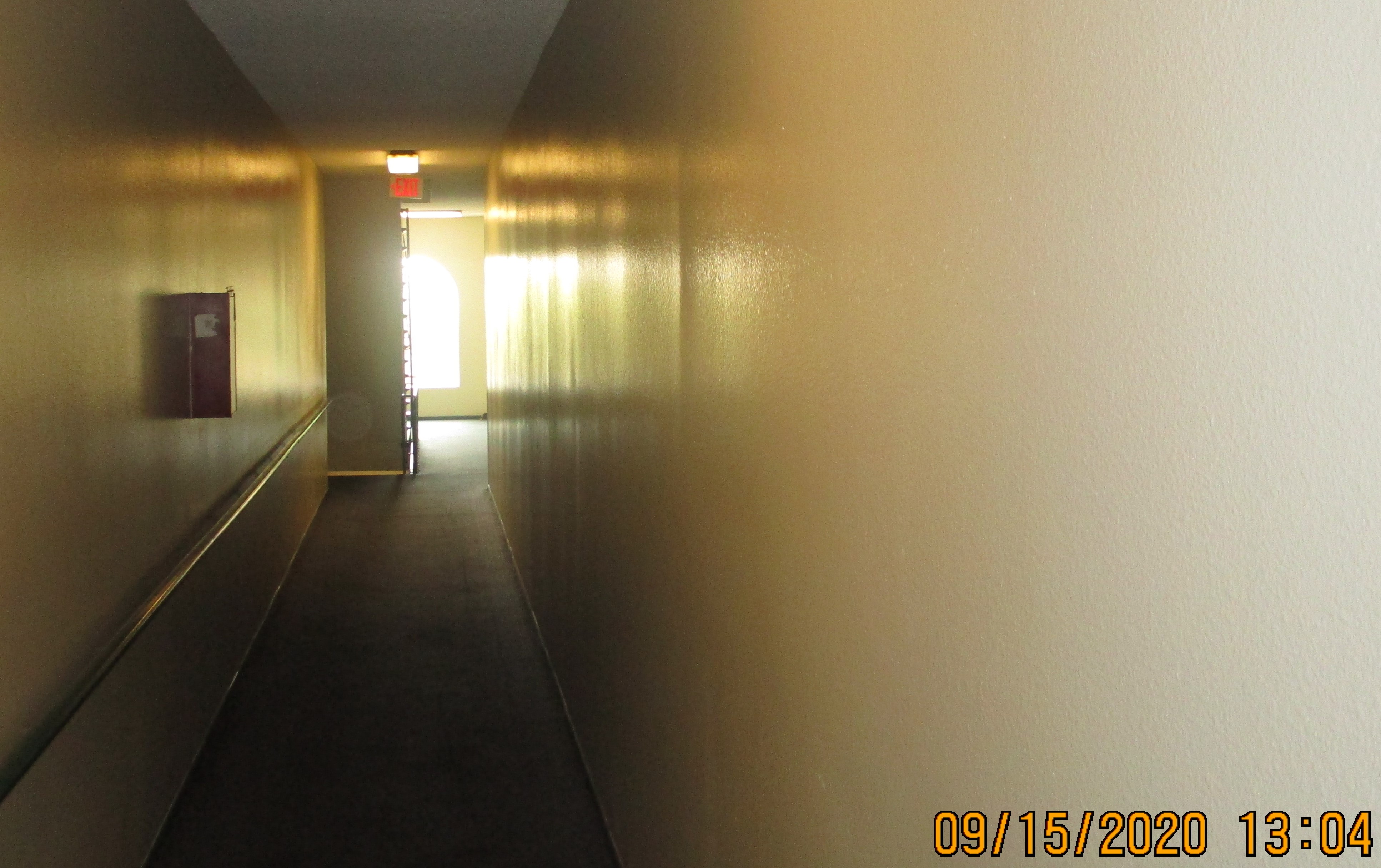 Image of an interior hallway with an exit sign at the end of the hall.