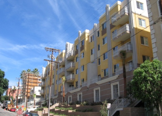 Five story yellow, brown and white building with bush garden in the front.