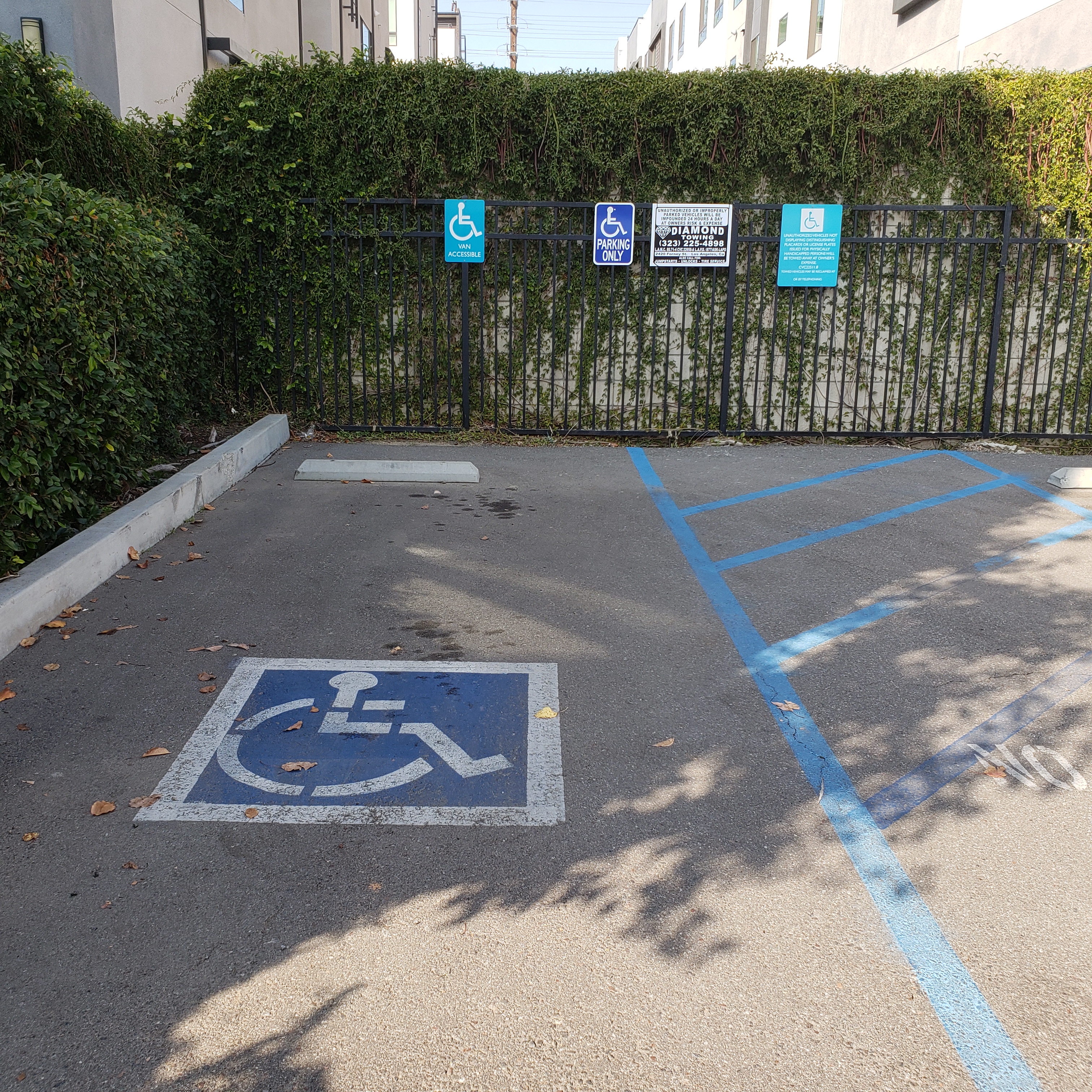 Image of tres lomas garden apartments accessible parking area. accessibility symbol painted in blue and signs posted on gate marking accessible parking area.