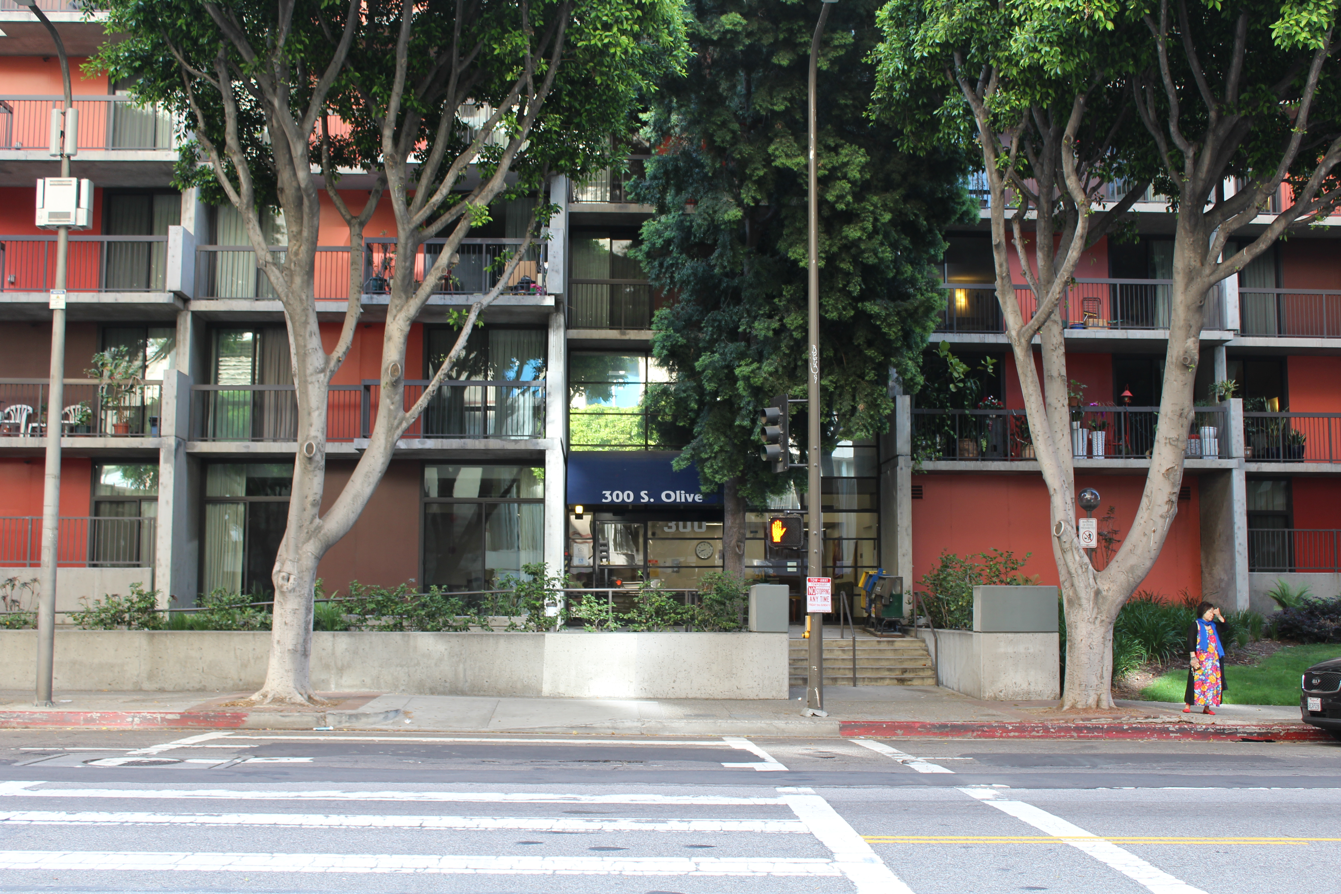Street view of Angelus Plaza 1. Multilevel orange building with large trees and street lamps on sidewalk in front of builing.