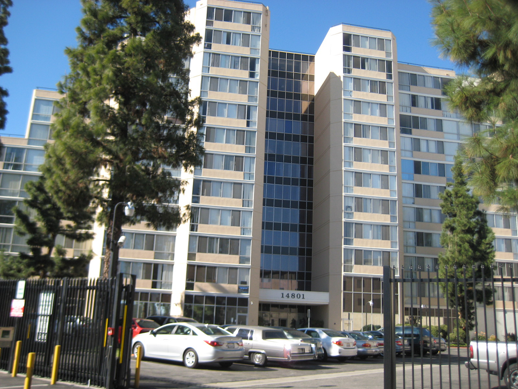 Large twelve story building with large windows. There is gated parking in front of the building.