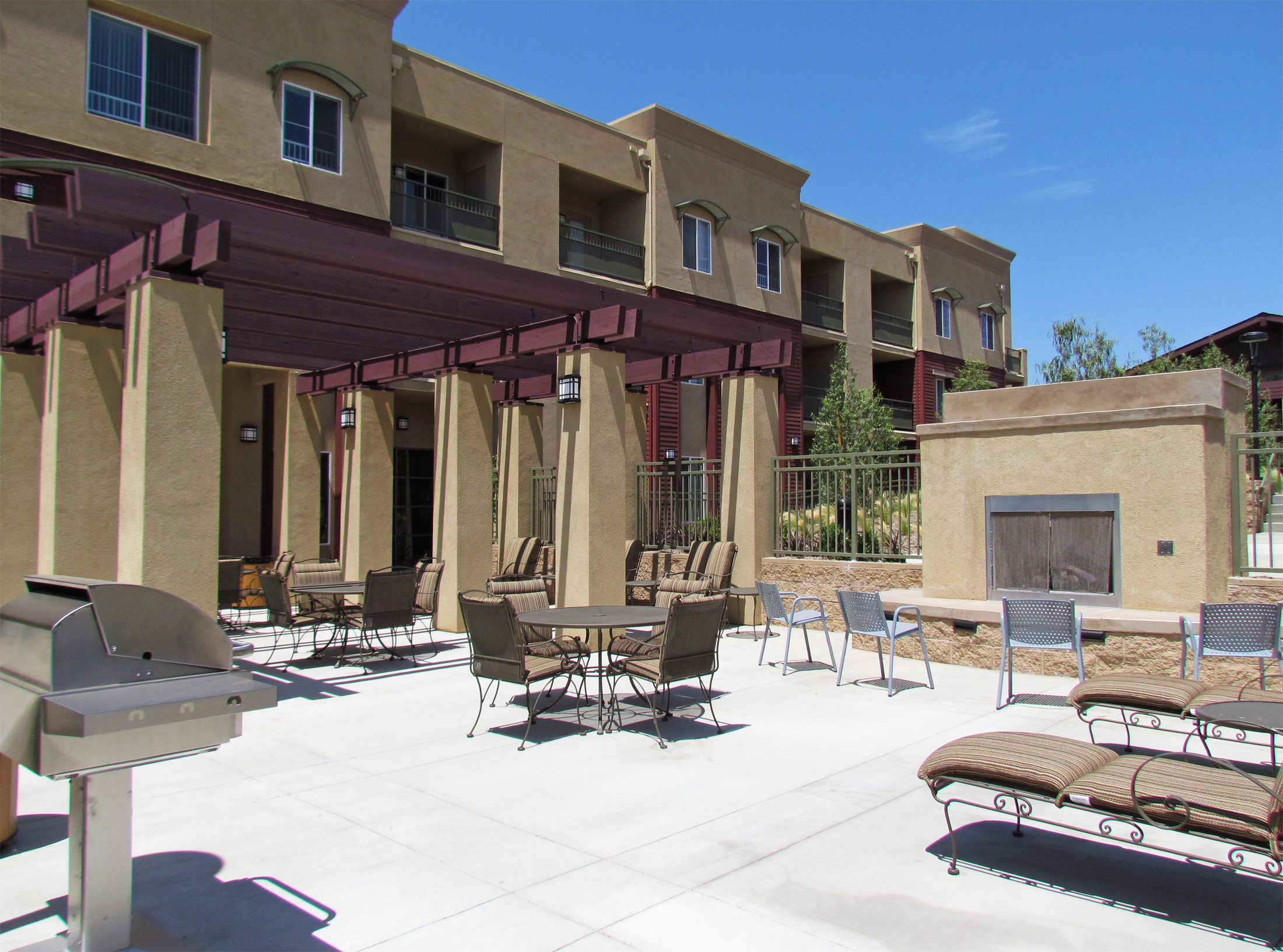 Exterior view of the patio area at Osborne Street Apartments. Tables, chairs, lounge chairs, fireplace, and a barbeque