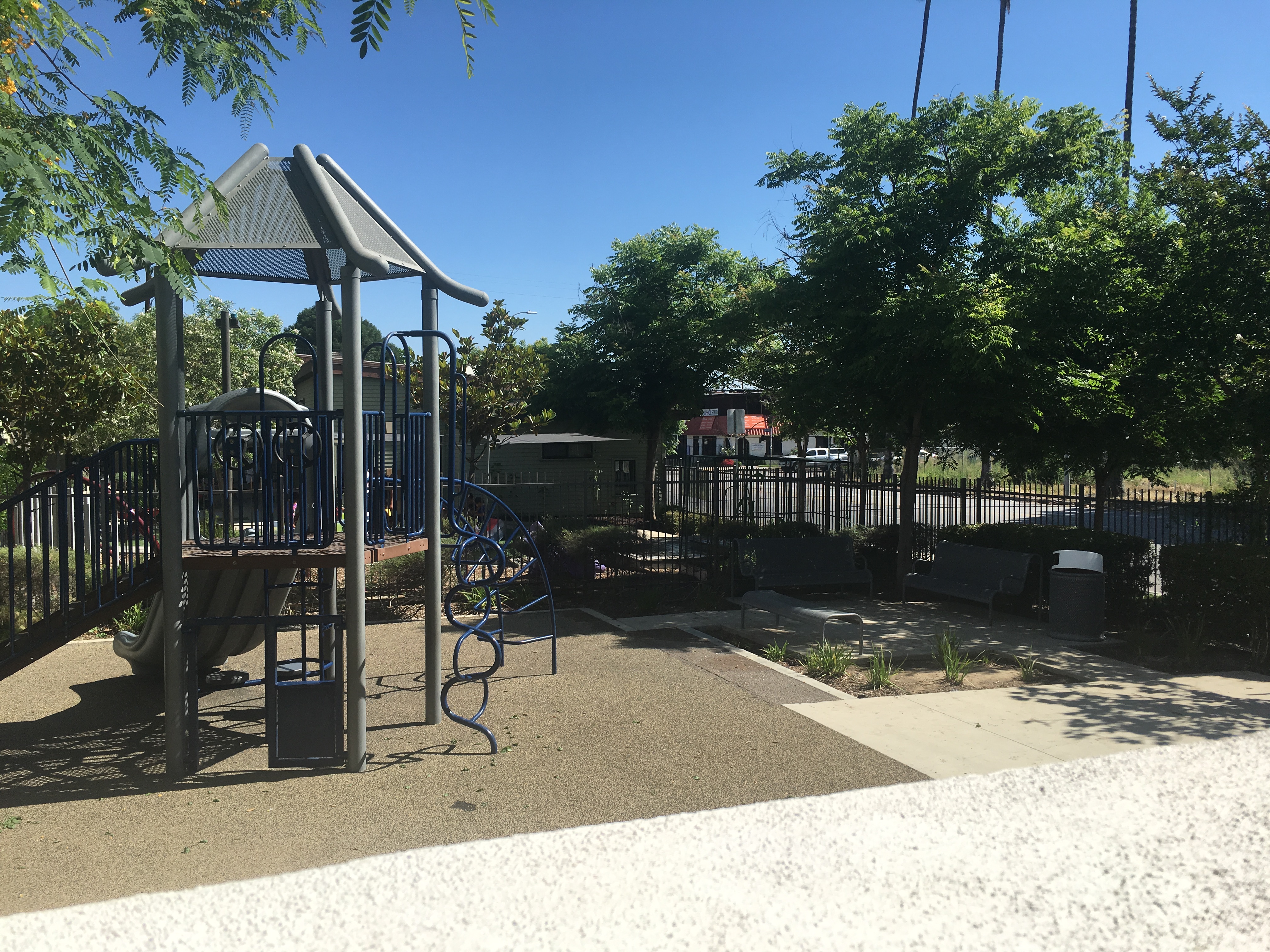 View of a gated playground, benches and trees all around.