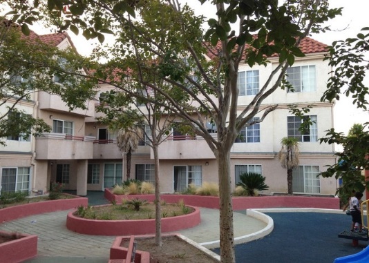 Courtyard with trees and plants. There is a playground adjacent to this area. Building is three floors.