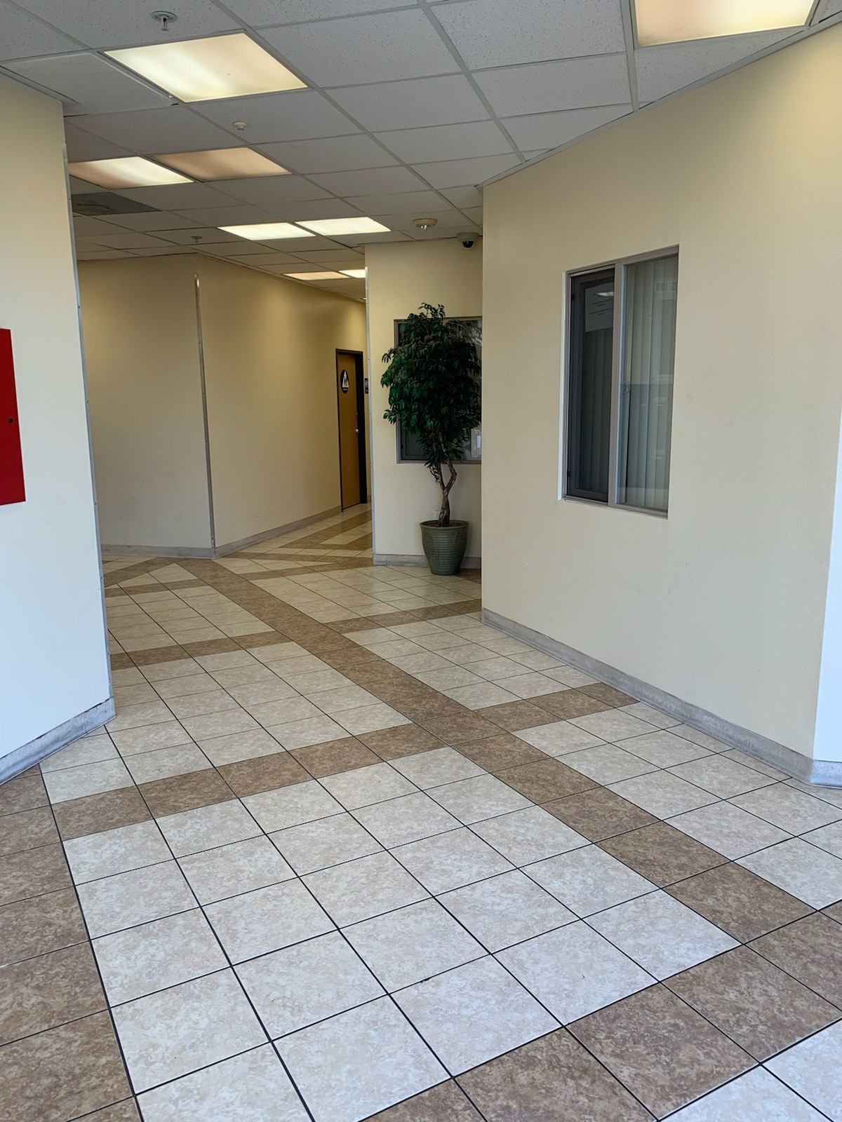 Lobby area with a reception window, a floor plant, and a gender neutral restroom in the back. Floor is tiled.
