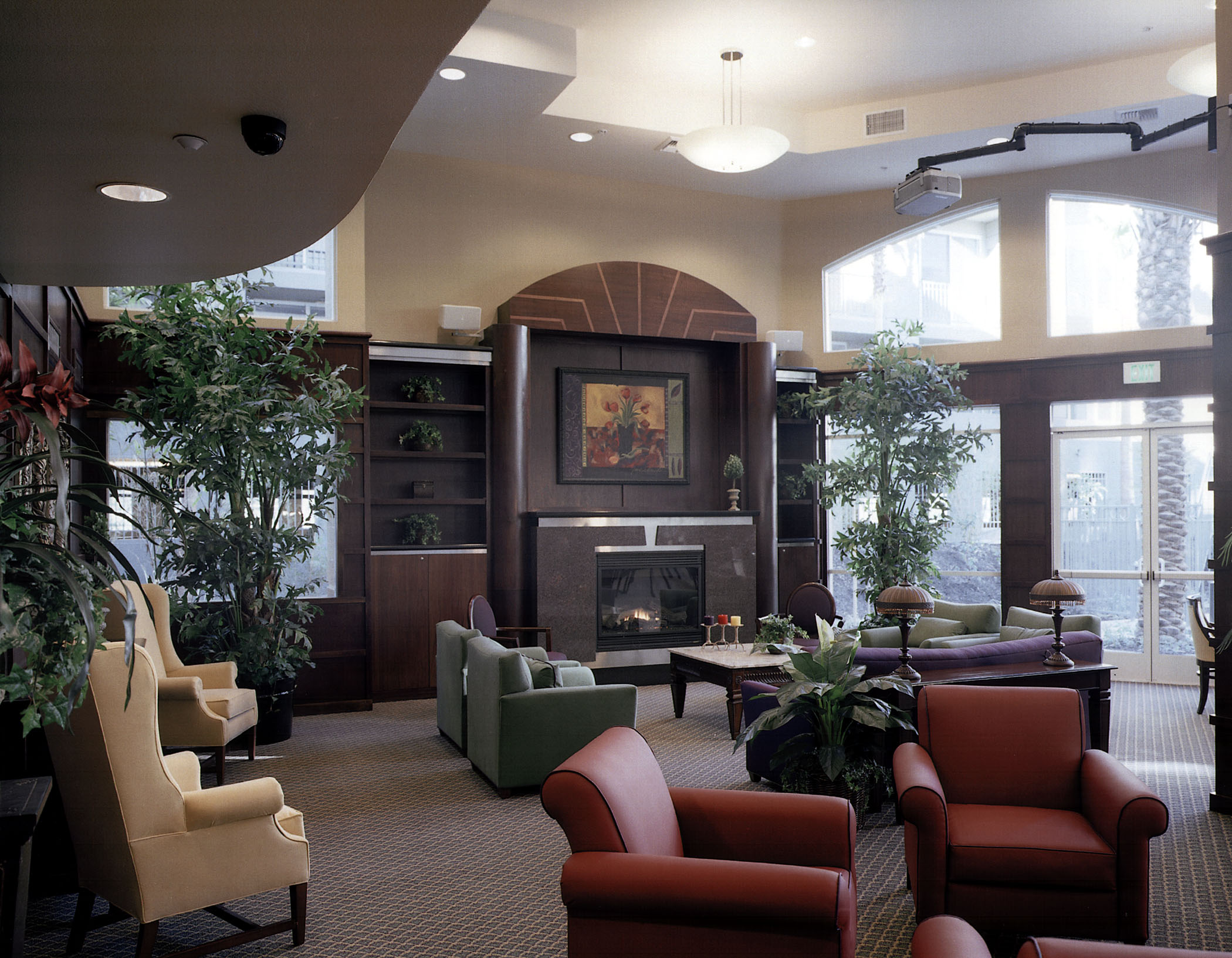 Indoor view of a lobbying area. There is a modern fireplace surrounded by a variety of sofas and plants.