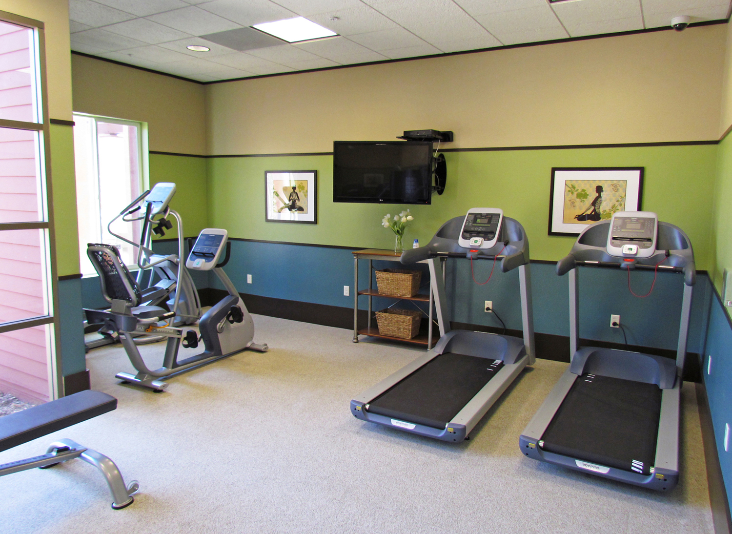 Interior view of a fitness room at Osborne Street Apartments. three different machines with a television attached to the wall