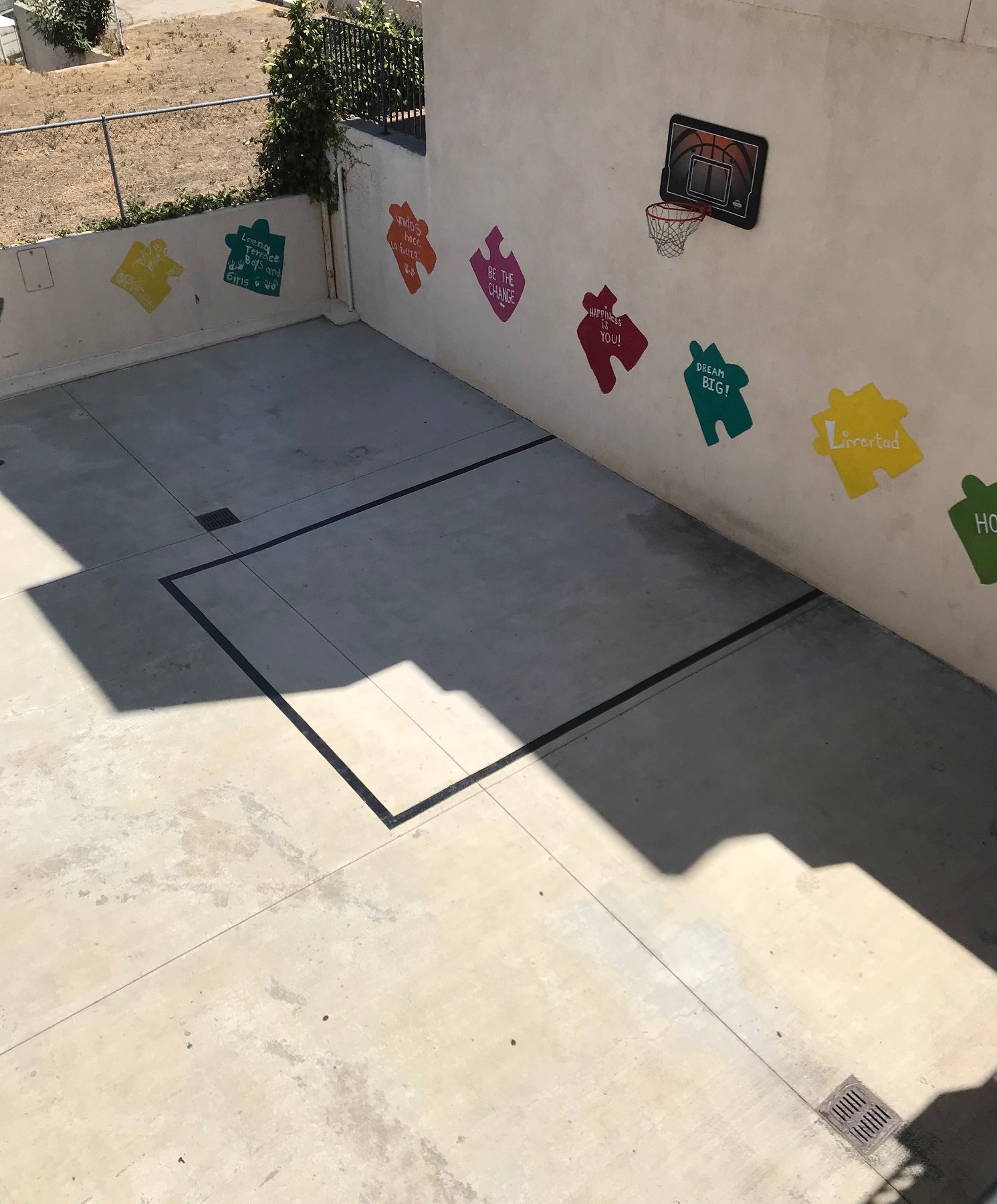Exterior view of a basetball court at Lorena Terrace with large colorful puzzle piecies painted on the walls