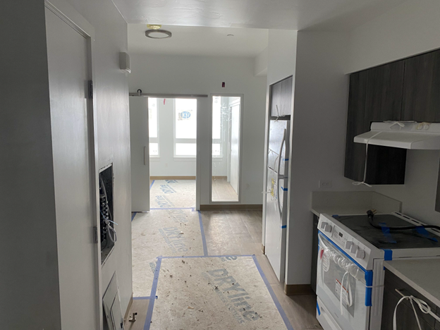 Unit entrance, walls white, right kitchen cabinets, range and refrigerator. Straight ahead bedroom