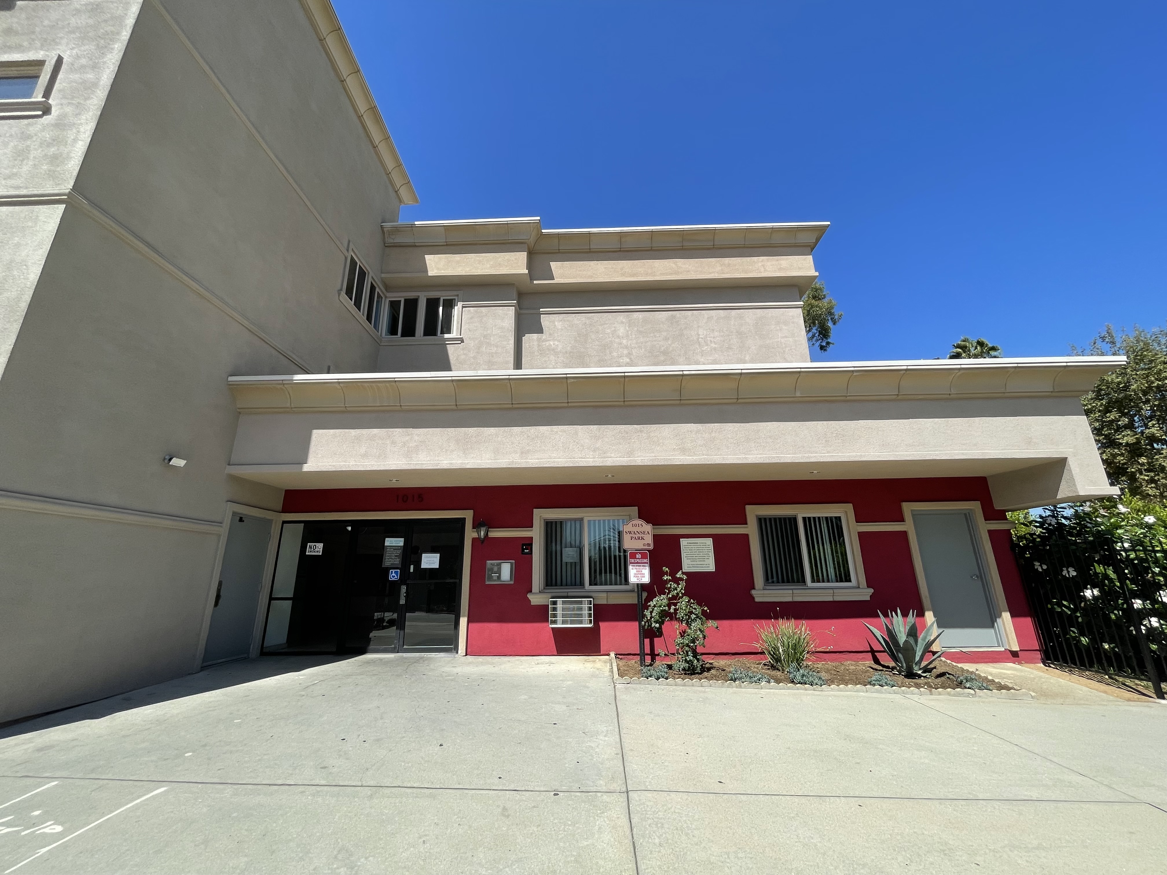 Photo showing the outside of the building entrance. Outside wall is red. Outside entrance also has windows and a glass door.