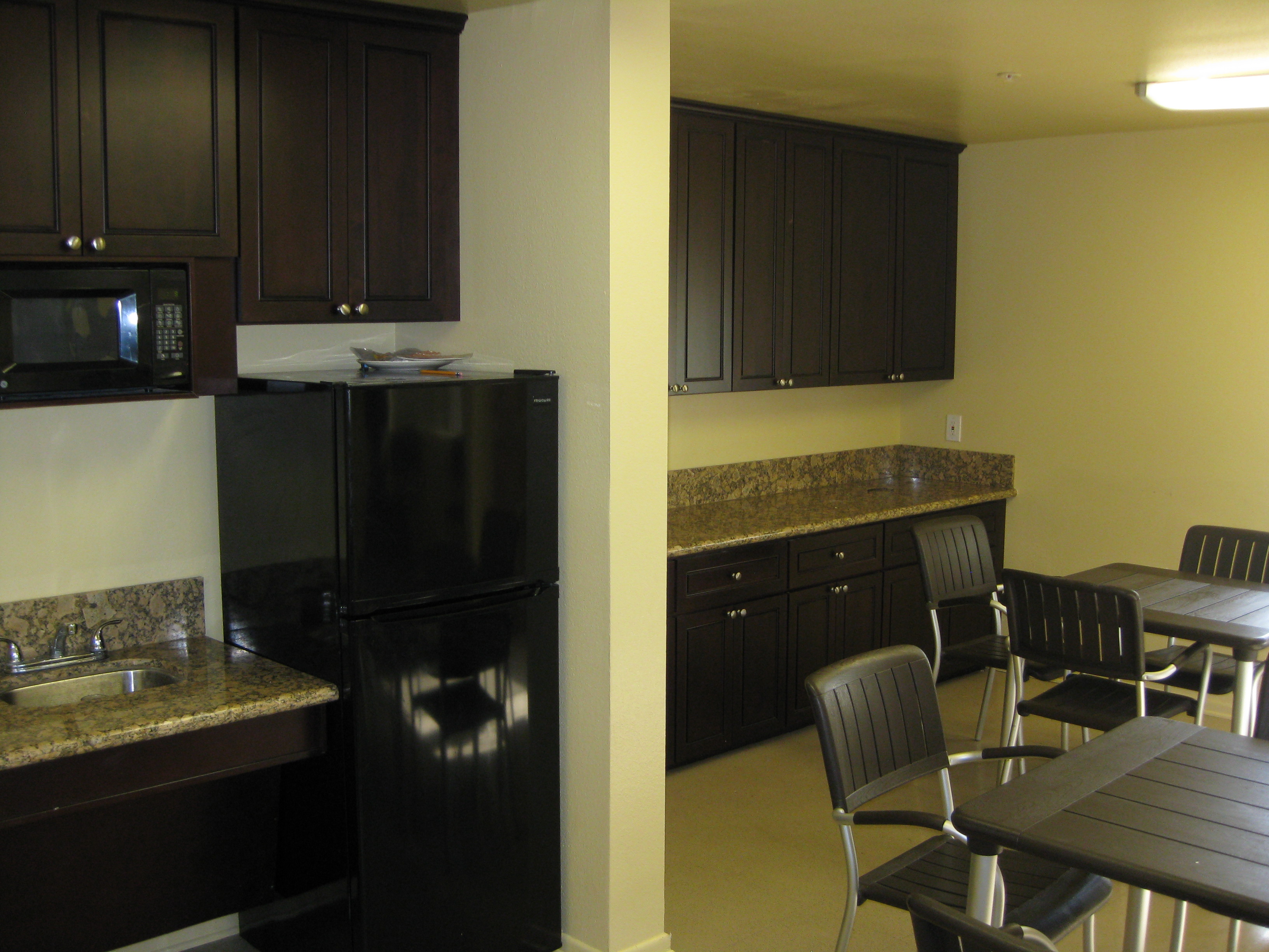 Paradise arms common area. community kitchen with long counter tops, fridge, sink, microwave, tables, and chairs