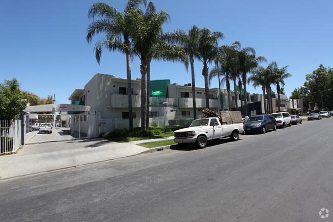 Street view of Alabama Apartments with a gated parking area along side of the building and tall Palm trees in front with cars park along the street