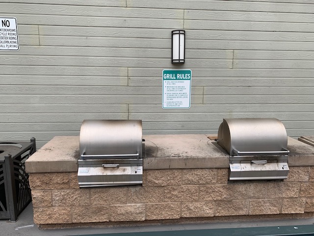 Two stationary BBQ grills and a trach bin next to them