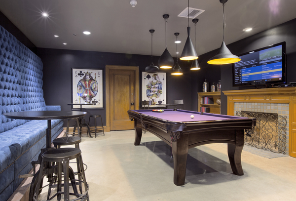 Interior view of billiard game room with Television, tall cocktail tables, stools and unlit fire place at Gas Company Lofts