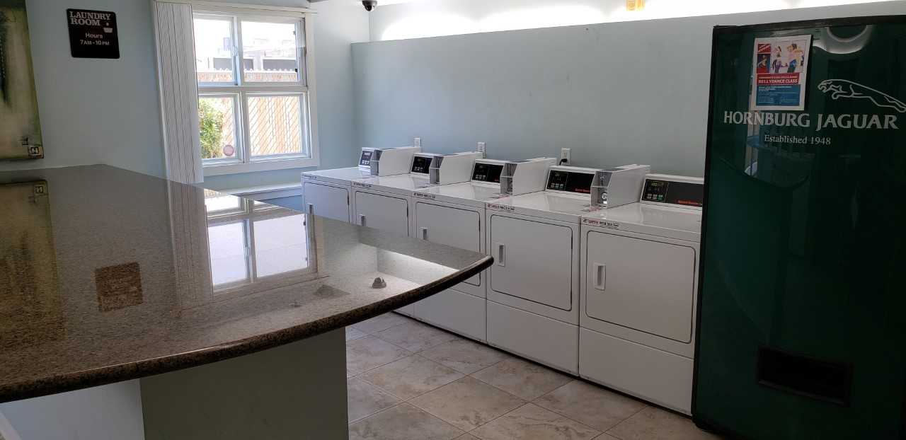 Image of Rayen Apartments laundry room. Large island near center of room. Five dryers along wall. beverage vending machine available.