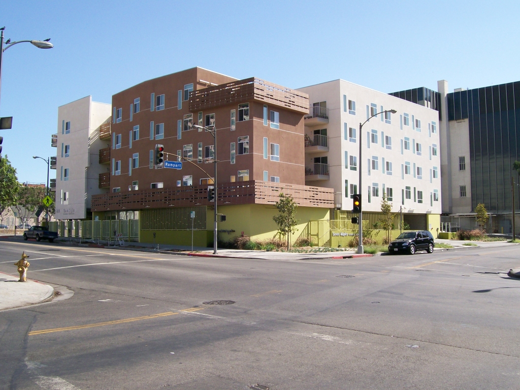 Street view of four story dual building apartments in brown, green and white color. Apartments include balcony and a terrace