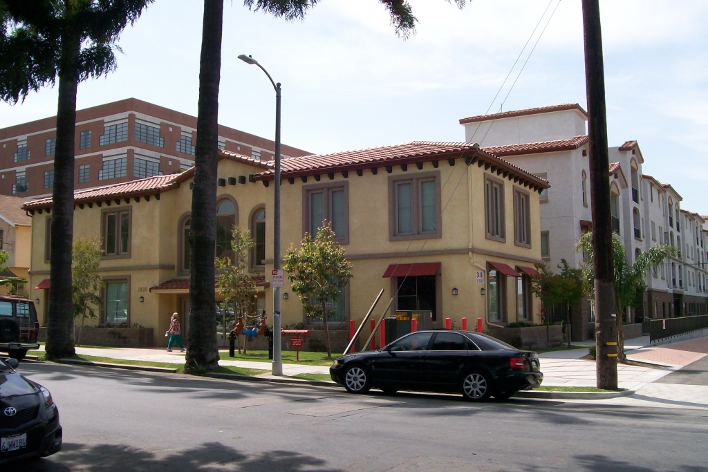 Street view of yellow 2 story apartment with grass, sidewalk and palm trees in front