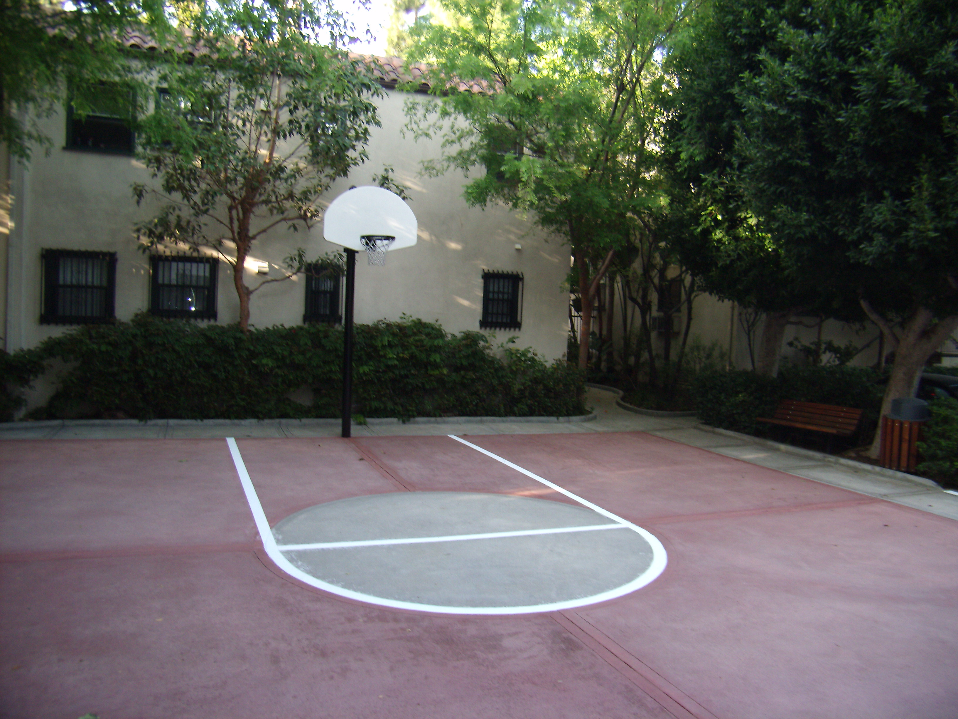 Exterior view of Hollywood El Centro Apartments basketball court. The building is behind the court with trees and bushes dividing the space between.