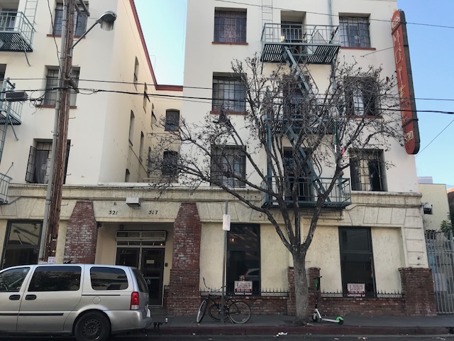 Street view of Russ Hotel with brick columns leading to the entry way and a large tree on the side walk with a van parked on the street.