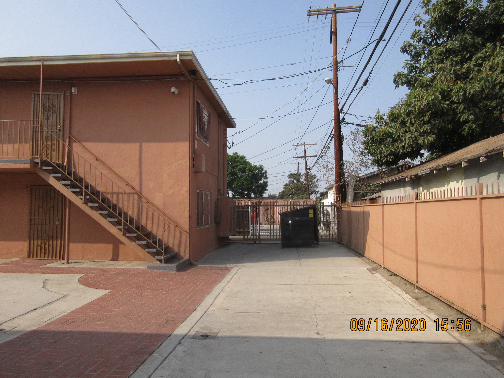 View of a patio, all concrete, big trash bin.