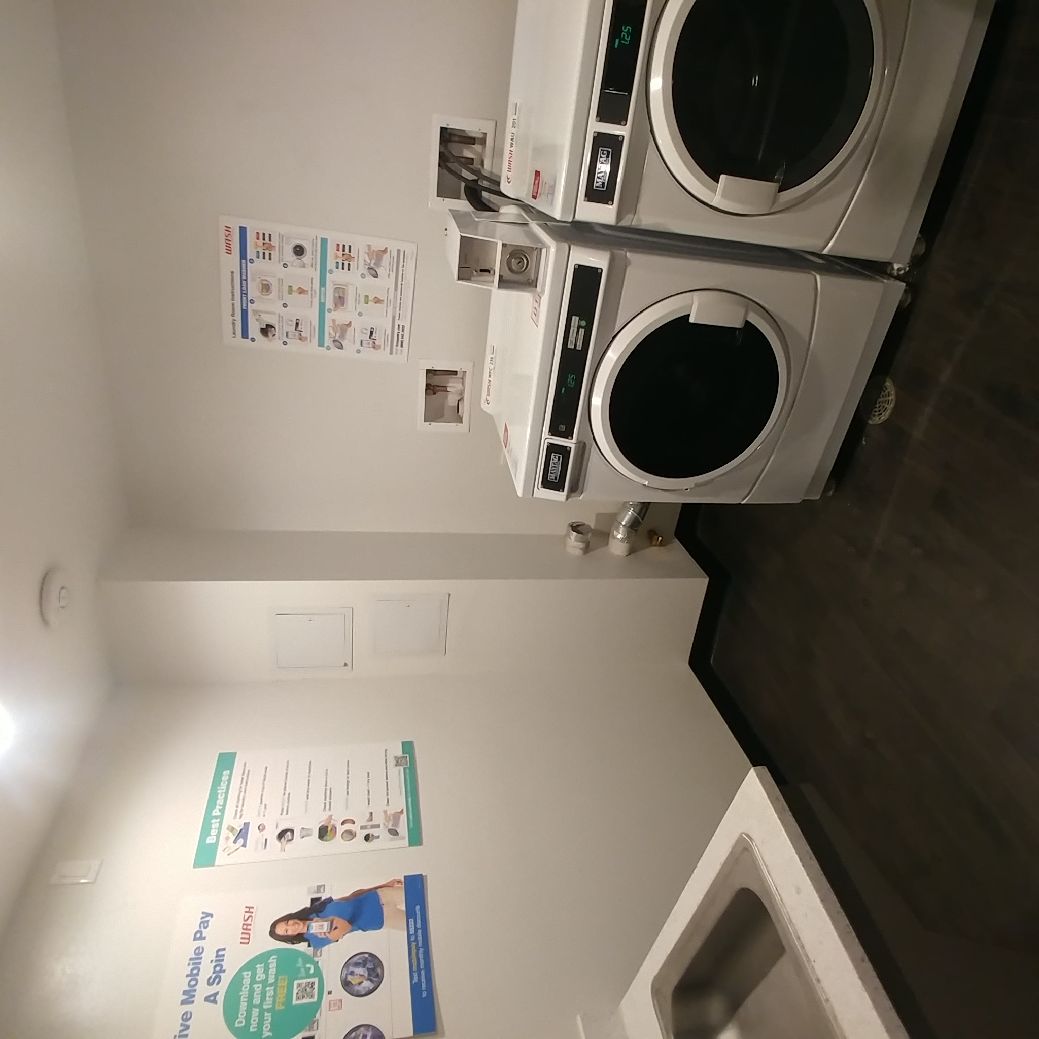 Panama Apartments laundry room. image contains two front load washing units, sink, and operating signs posted on wall