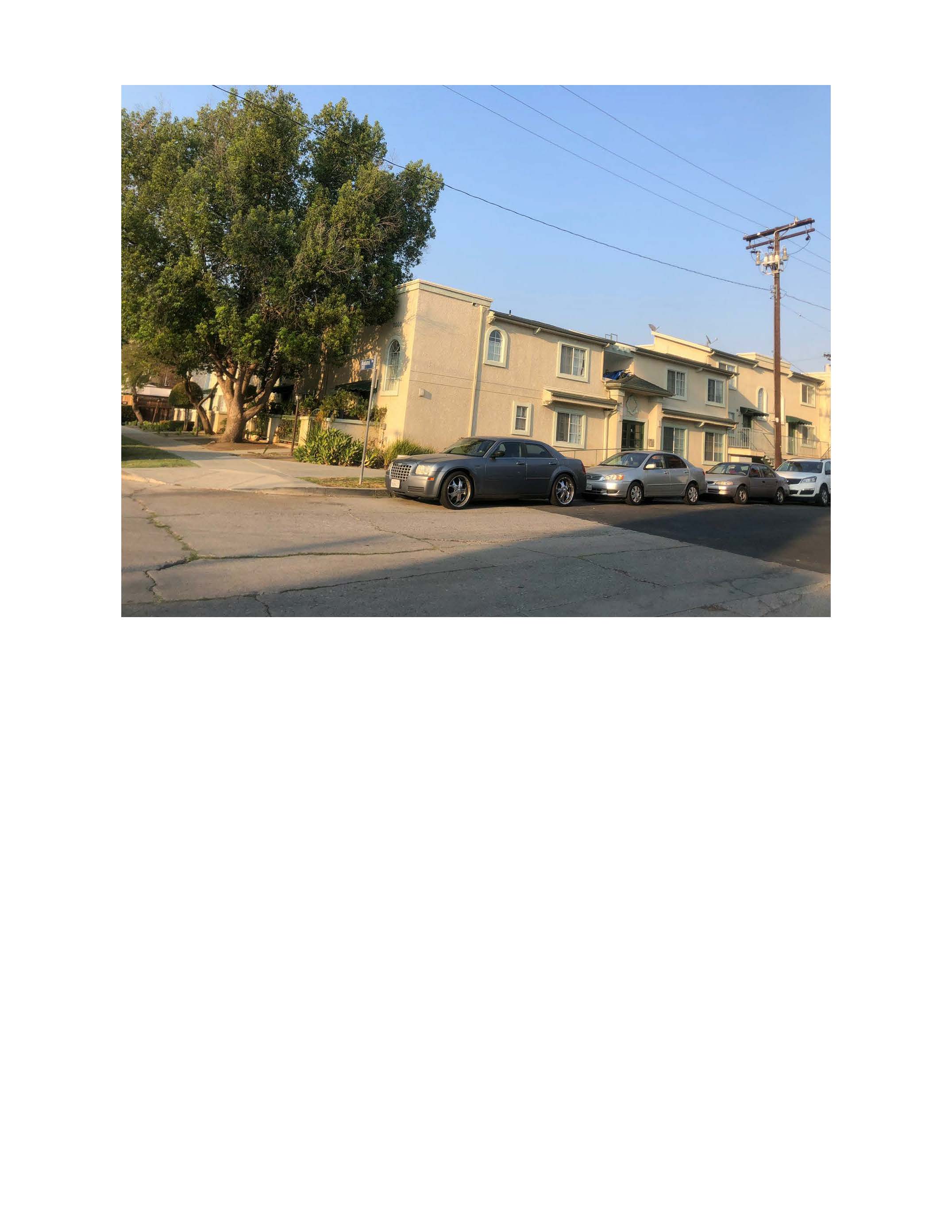 Photo of Street view of a one story apartment building, with cars parked on the side of the road.