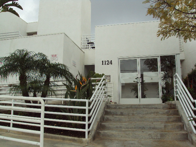 Front view of the main entrance, two glass door entrance, call box on the left side, aa24 building number on the left side, white handrails.