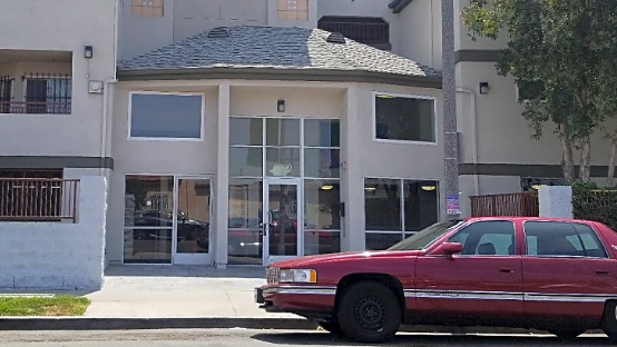 Front view of apartment building entrance, large glass windows, red car parked in front of building