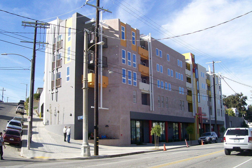 Corner view of tan 5 story family housing building with balconies and street parking along the sides of the building