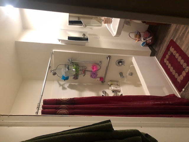 View of bathroom. Shower tub with multiple grab bars. One over the head stationary shower head along with a hand held shower head.