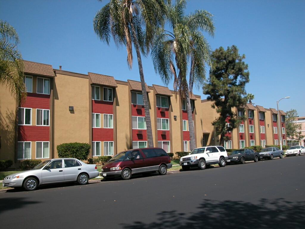 Image of 3 story building with shrubs and bushes along the side of hte building and trees in the front