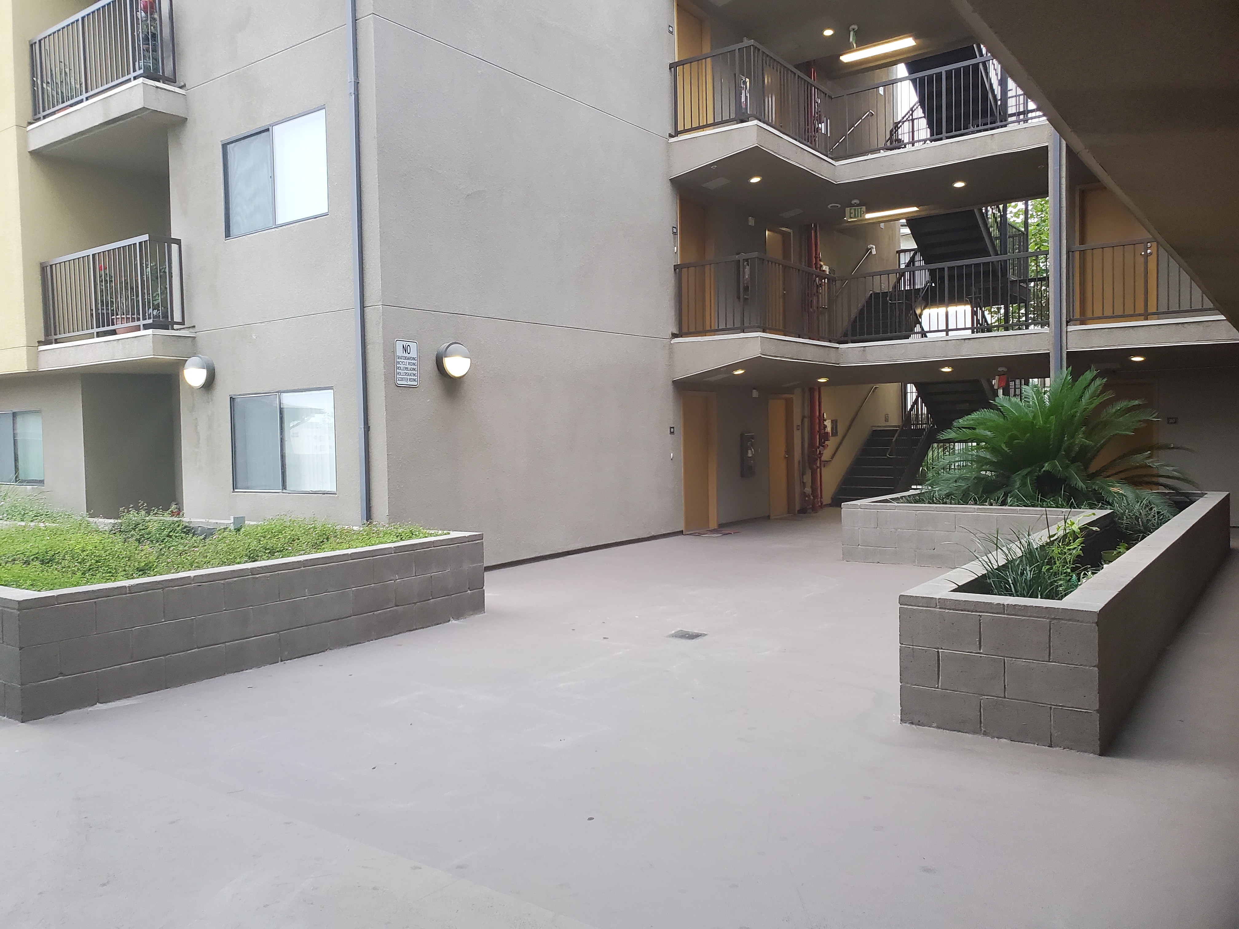 Side view of a courtyard, big concrete planters, stairways with handrails and security fence.