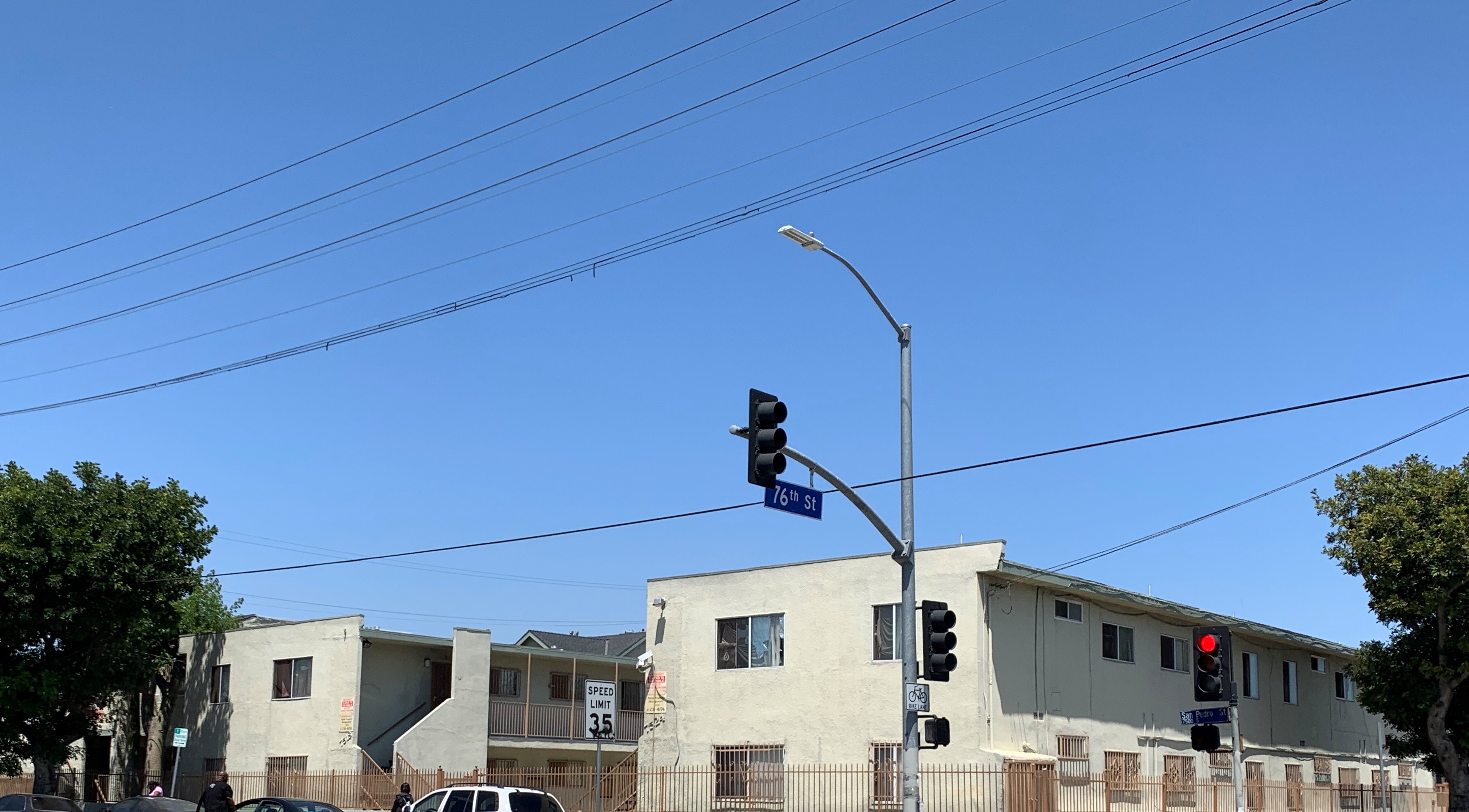 Corner of 7th and San Pedro street view, traffic light signals, two beige two story buildings, multiple windows, all gated, stairs with iron handrails, no public parking and management company signs, white with black letters 35 speed limit sign, bike lane