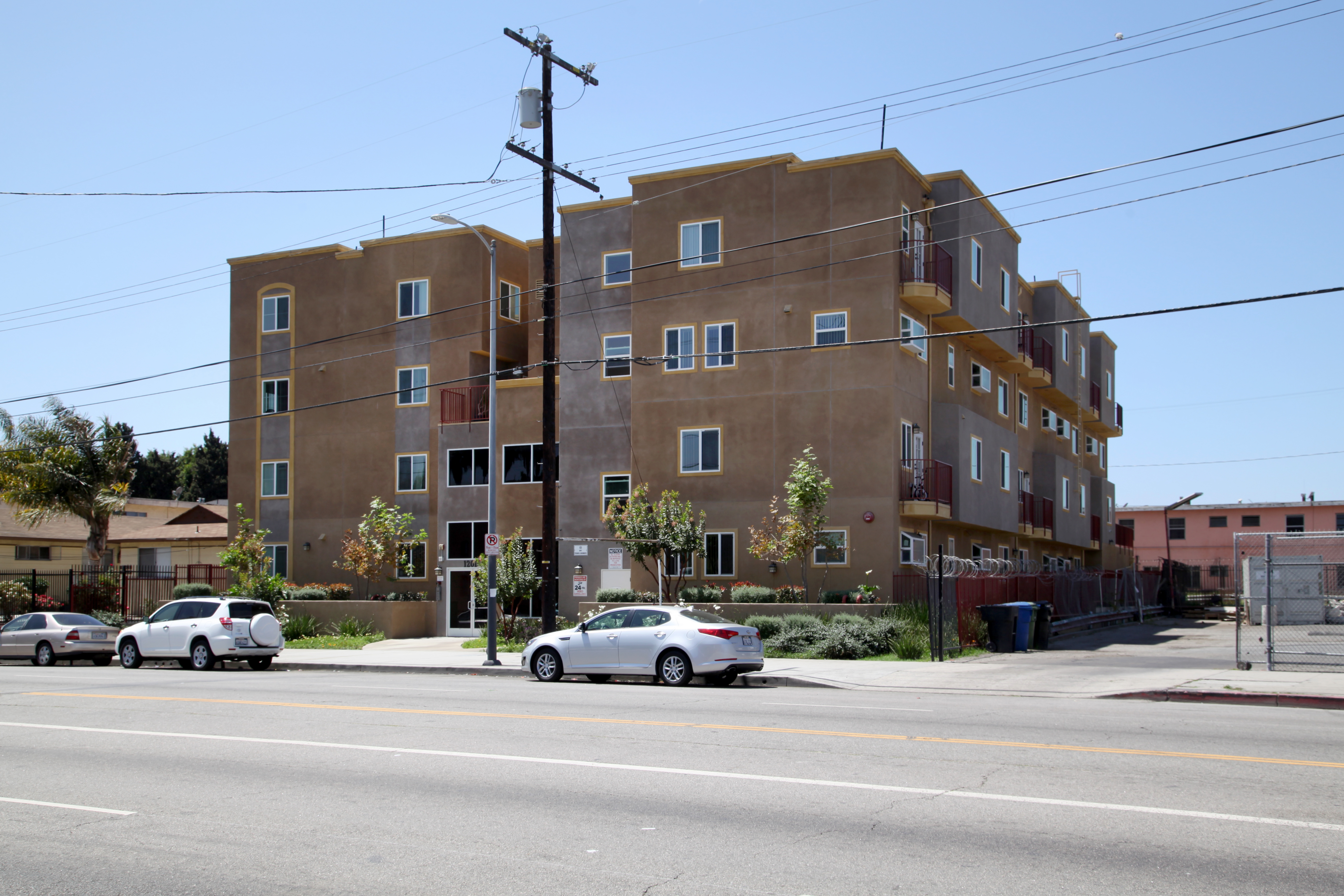 Street view of a three story brown building with car parking adjacent to the property
