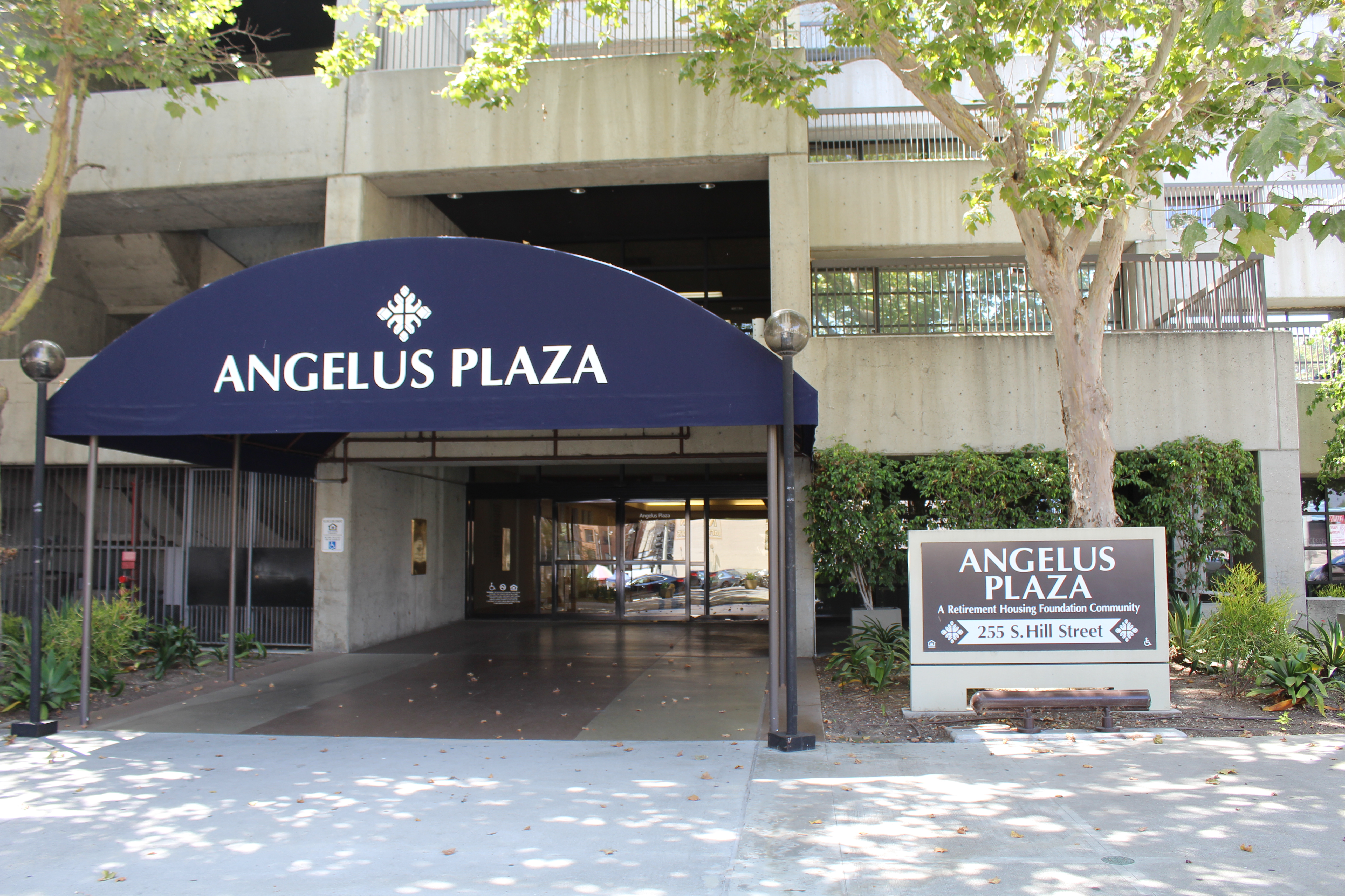 Close-up street view of the entrance to Angelus Plaza 1. Navy blue awning with white lettering covering the walkway to the building entrance