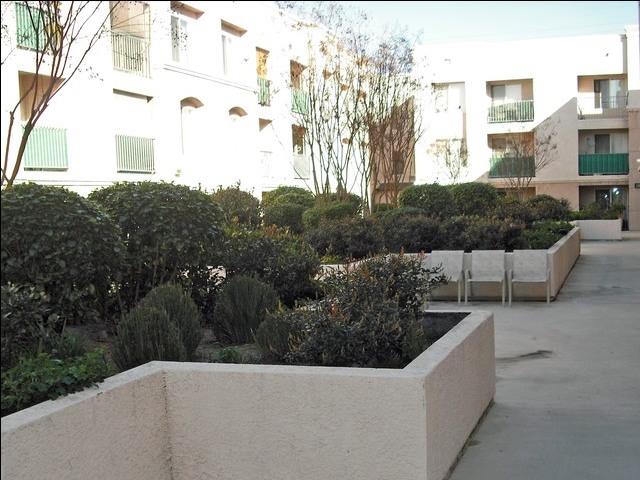 Side view of a courtyard, big concrete planters. Chairs in the center and three story building surrounding the courtyard.