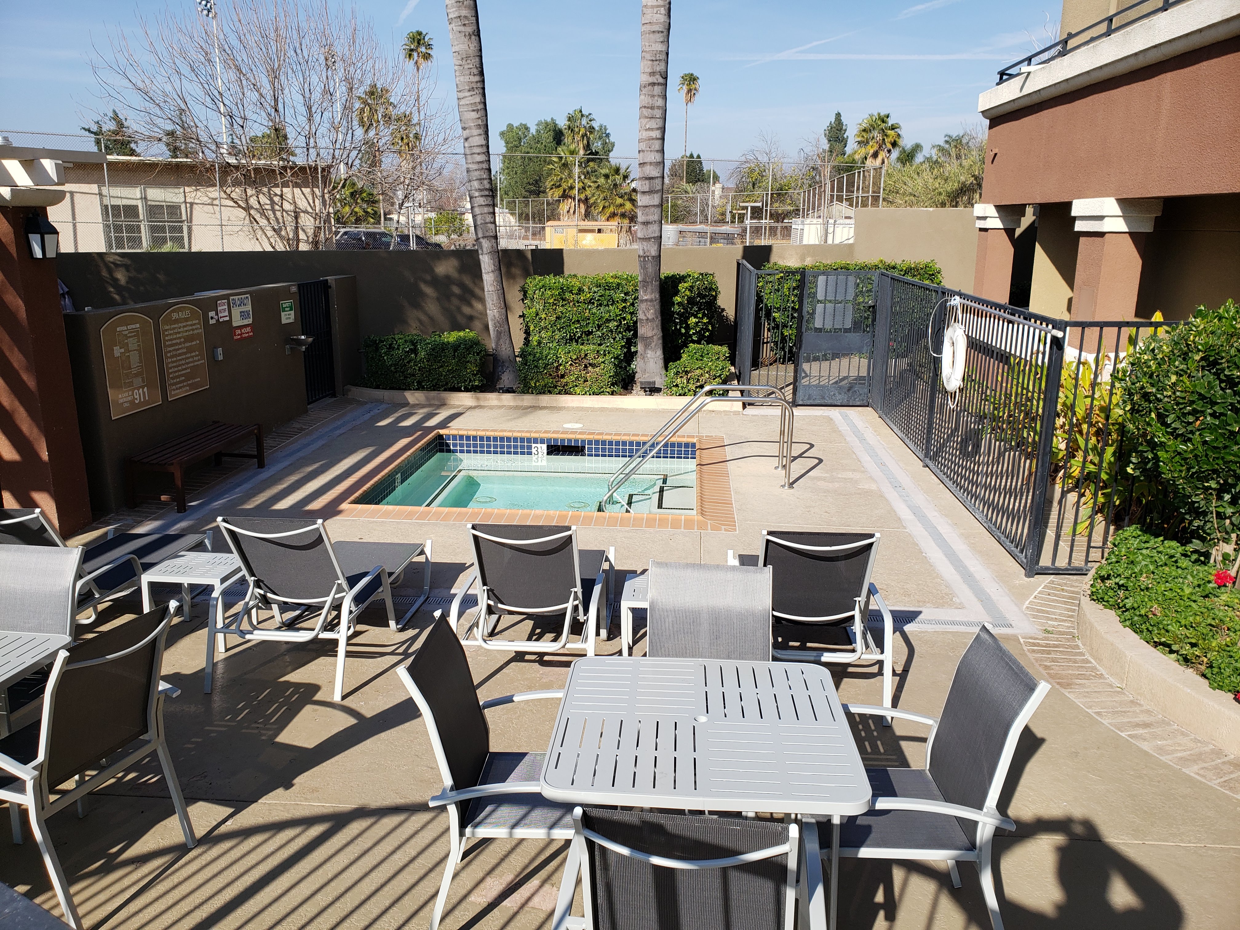 Image of vintage crossing senior apartments outdoor spa area. Are is fenced off. spa located near bushes and palm trees. Pool shairs next to spa.